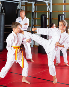 Children sparring in a martial arts class with an instructor observing in the background, guiding their technique and focus.