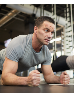 A man performing a forearm plank on a gym mat, maintaining a straight line from head to heels with proper form.