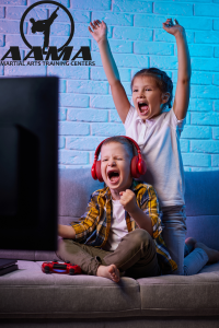 Two excited children cheer while playing video games on a couch, illustrating the importance of balancing screen time with how to build real-life confidence in kids.