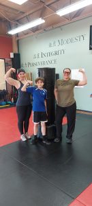 Mother, son, and friend flex their muscles beside the heavy bag after finishing modifications during the Memorial Day Murph Workout
